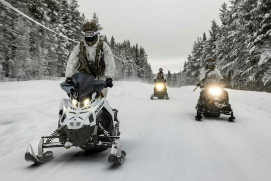 Military personnel travelling by snowmobile during cold weather training